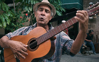 Un hombre con un sombrero tocando la guitarra en la calle.