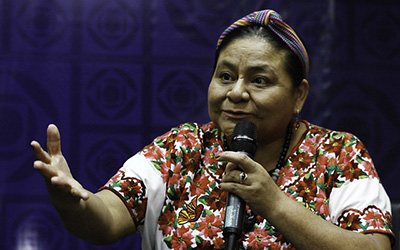 Rigoberta Menchú con vestimenta tradicional indígena con un micrófono en la mano.
