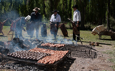 Cuatro hombres en el campo haciendo un asado. Las parrillas al aire libre están llenas de chorizos y morcillas.