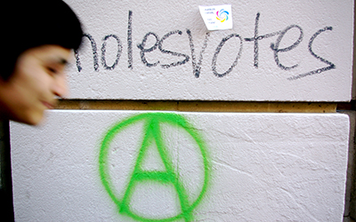 Una pared blanca que dice, “nolesvotes” y una “A” con un círculo alrededor.