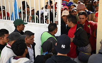 Centroamericanos tratando de pasar por una reja de metal blanca.