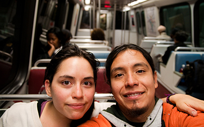 Un hombre y una mujer tomándose un selfie en el coche de un tren que tiene asientos rojos y azules.