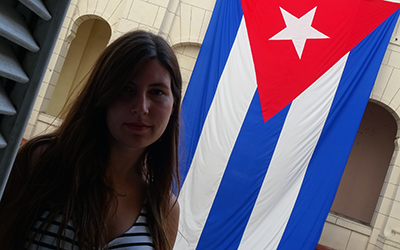 Una mujer en frente de una bandera cubana colgada de un edificio.