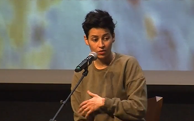 Denice Frohman vestida de verde en un escenario con un micrófono.