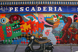 Hay una motocicleta enfrente de un mural muy colorido que cubre el protector metálico de una pescadería en la calle Noviciado en Madrid, España.