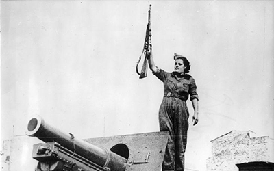 Una mujer encima de un cañón alza un arma.