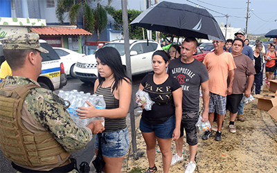 Una cola de personas esperando recibir agua y otros suministros de un soldado.