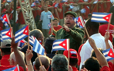 Fidel Castro en uniforme verde rodeado de personas con banderas cubanas en sus manos.