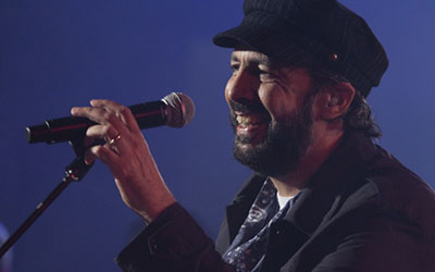 Juan Luis Guerra vestido de negro en primer plano cantando a través de un micrófono.