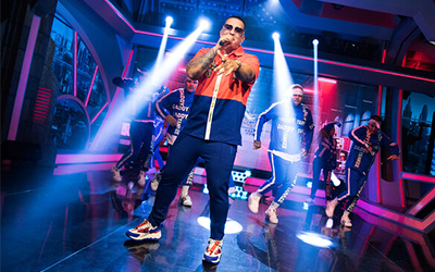 Daddy Yankee cantando en un escenario con luces con bailarines que llevan chándales detrás de él.