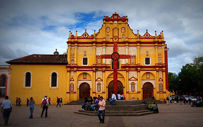 La Catedral de San Cristóbal de las Casas en Chiapas que es un edificio colonial amarillo y hay personas en la plaza en frente.