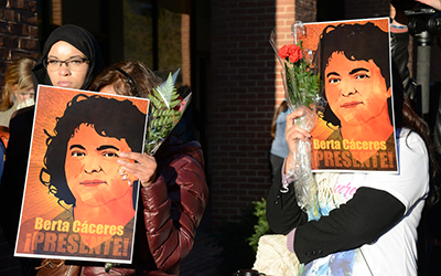 Persona en una manifestación con pancartas con la cara de Berta Cáceres que dicen “Berta Cáceres Presente!”