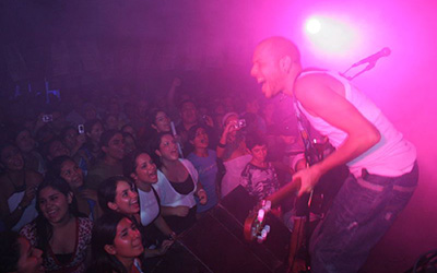 Un hombre cantando y tocando guitarra en un escenario en frente de muchas personas.