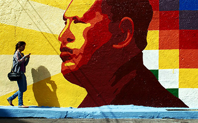 Un mural de Hugo Chávez y una chica caminando en frente.
