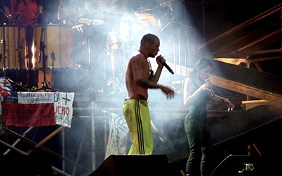 Calle 13 cantando en un escenario bajo una luz blanca.