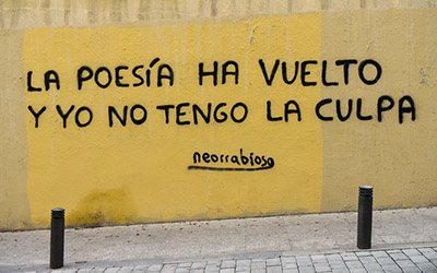 Una pared amarilla con texto que dice, “La poesía ha vuelto y yo no tengo la culpa neorrabioso”.